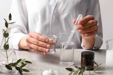 Scientist making cosmetic product at grey table in laboratory, closeup