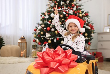 Cute little girl driving toy car in room decorated for Christmas