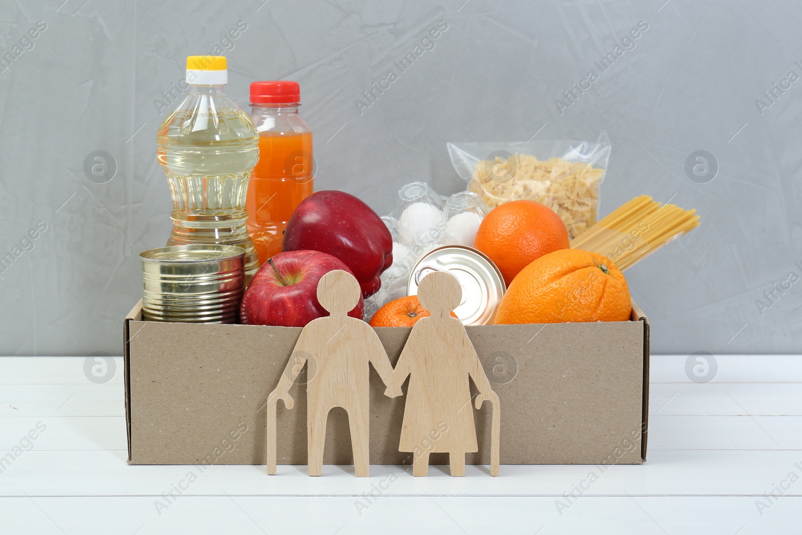 Photo of Humanitarian aid for elderly people. Different donation food products and figures of senior couple on white wooden table