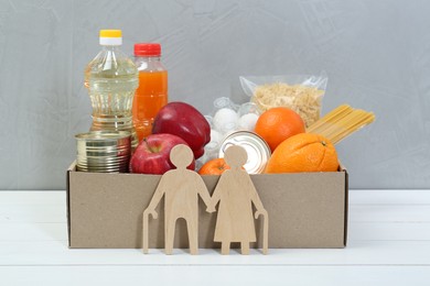 Humanitarian aid for elderly people. Different donation food products and figures of senior couple on white wooden table