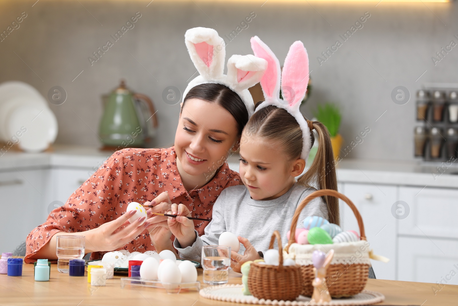 Photo of Mother and her cute daughter painting Easter eggs at table in kitchen