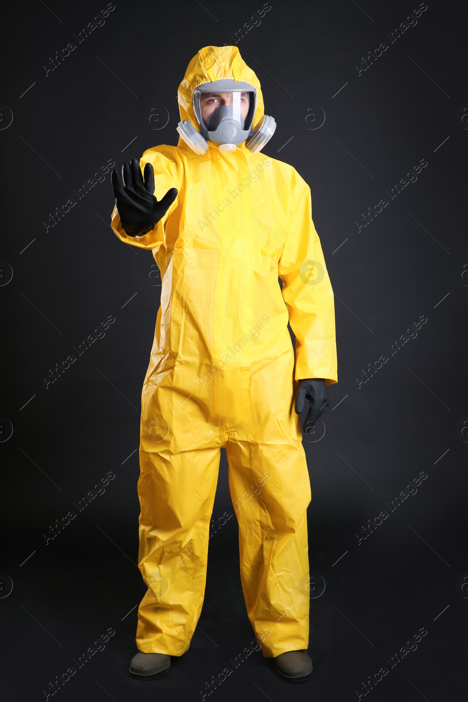 Photo of Man in chemical protective suit making stop gesture on black background. Virus research