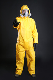 Photo of Man in chemical protective suit making stop gesture on black background. Virus research