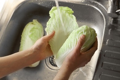 Photo of Woman washing fresh Chinese cabbages in sink, closeup