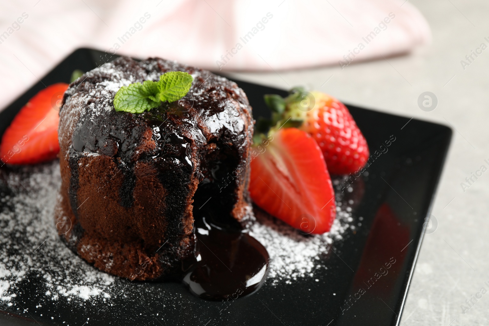 Photo of Delicious warm chocolate lava cake with mint and strawberries on plate, closeup