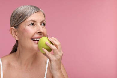 Photo of Beautiful woman eating fresh apple on pink background, space for text. Vitamin rich food