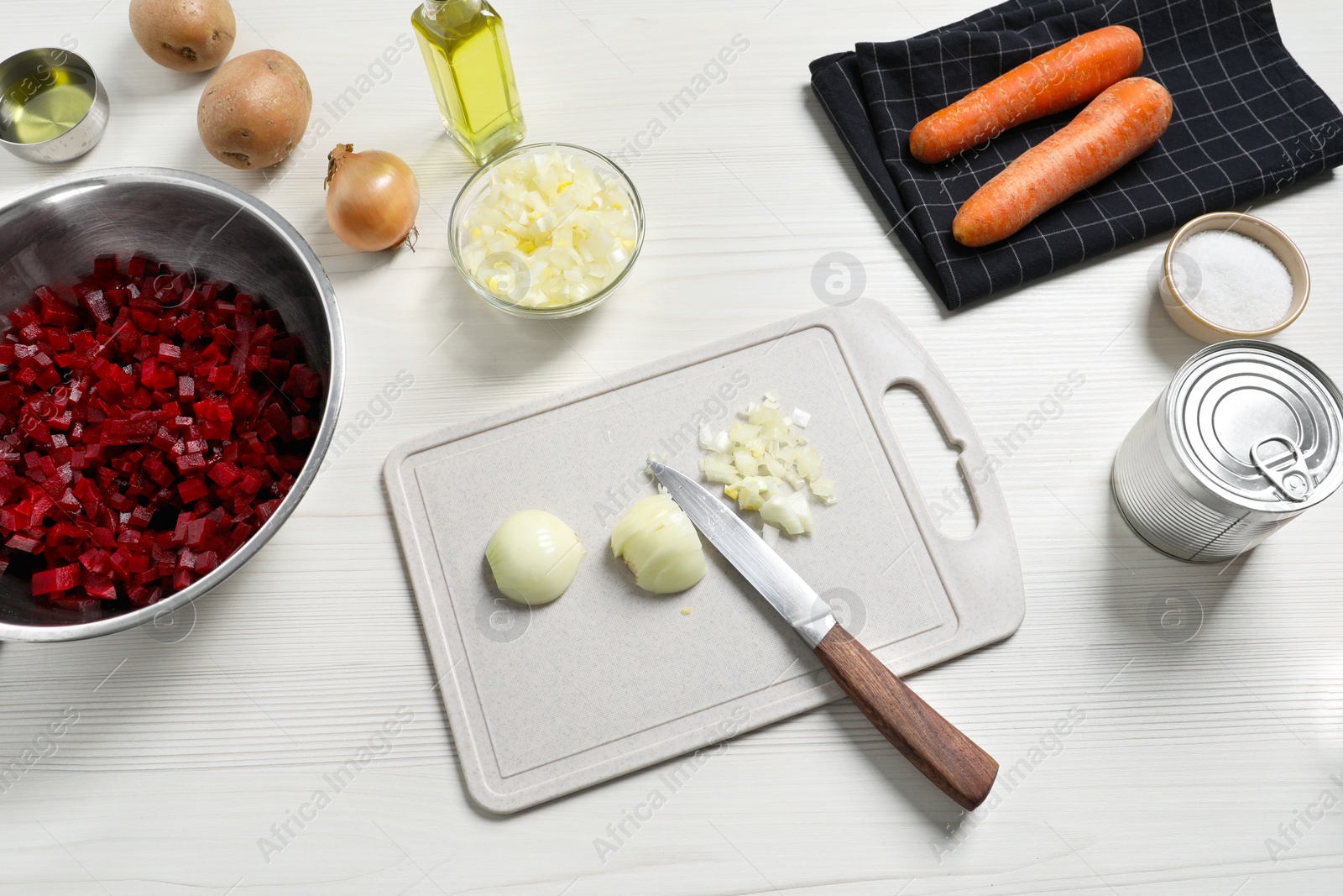 Photo of Cut onion and ingredients on white wooden table, above view. Cooking vinaigrette salad