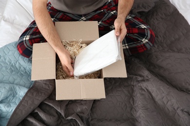 Photo of Young man opening parcel in bedroom at home, closeup
