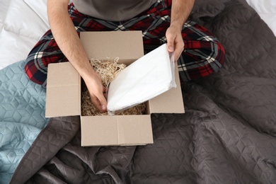 Young man opening parcel in bedroom at home, closeup