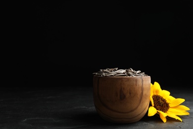 Photo of Raw sunflower seeds and flower on black table against dark background. Space for text