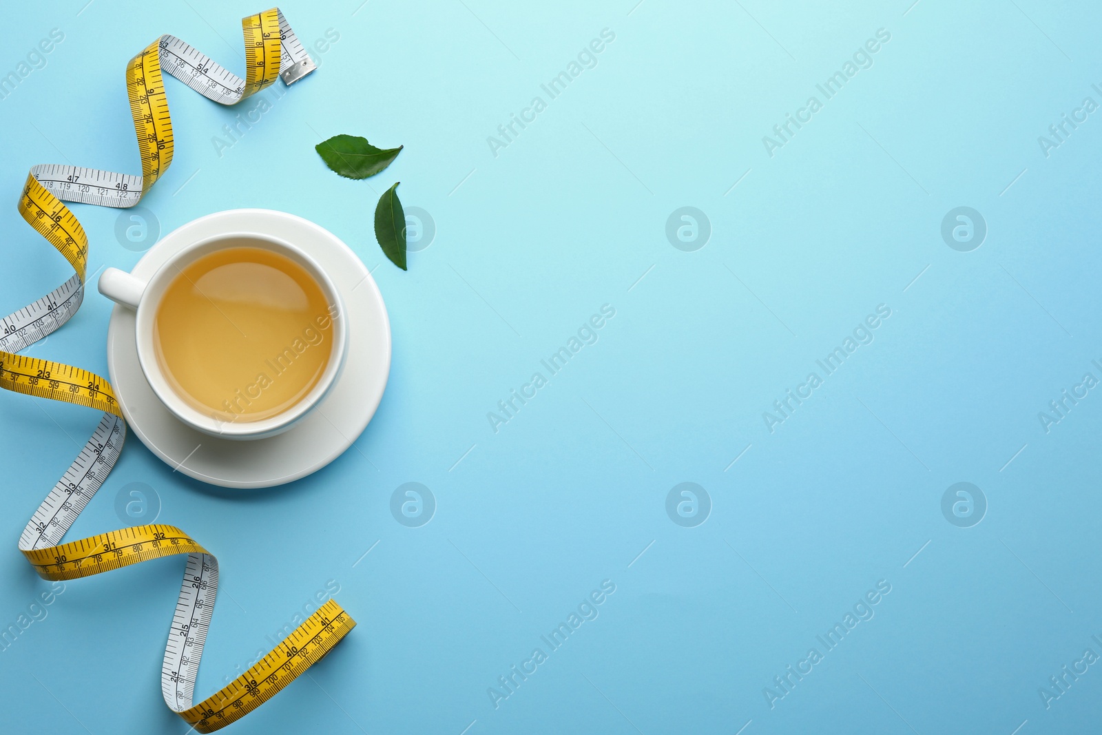 Photo of Cup of diet herbal tea, green leaves and measuring tape on light blue background, flat lay. Space for text