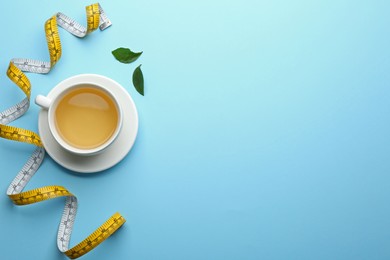 Cup of diet herbal tea, green leaves and measuring tape on light blue background, flat lay. Space for text