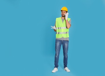 Male industrial engineer in uniform talking on phone against light blue background