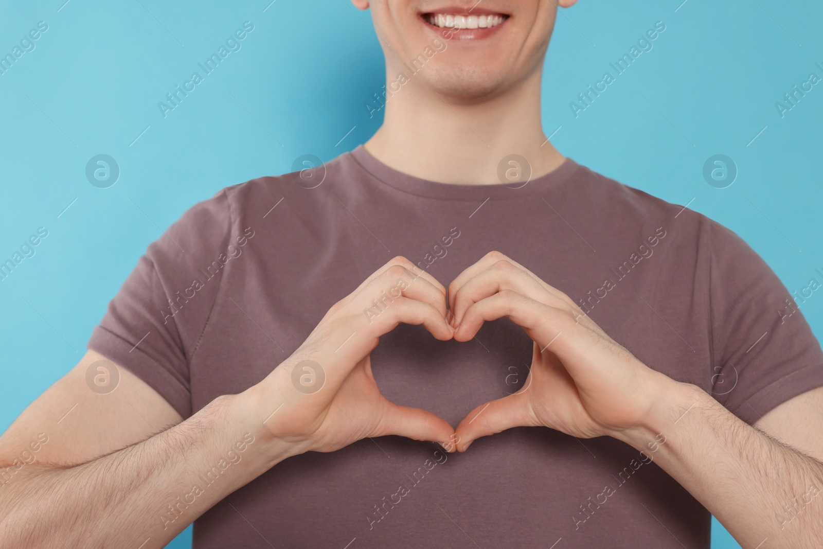 Photo of Happy volunteer making heart with his hands on light blue background, closeup