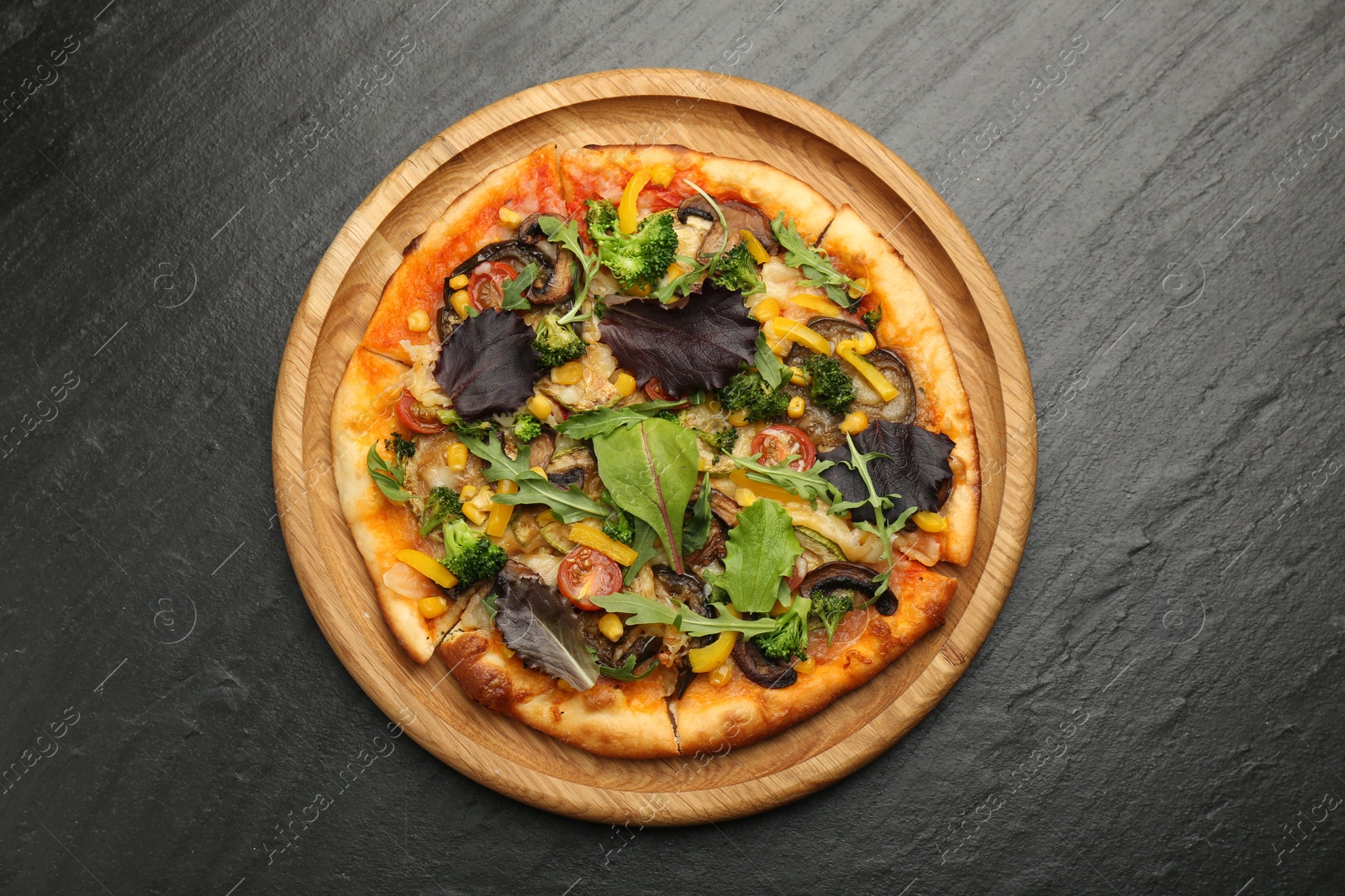 Photo of Delicious vegetarian pizza with mushrooms, vegetables and greens on black table, top view