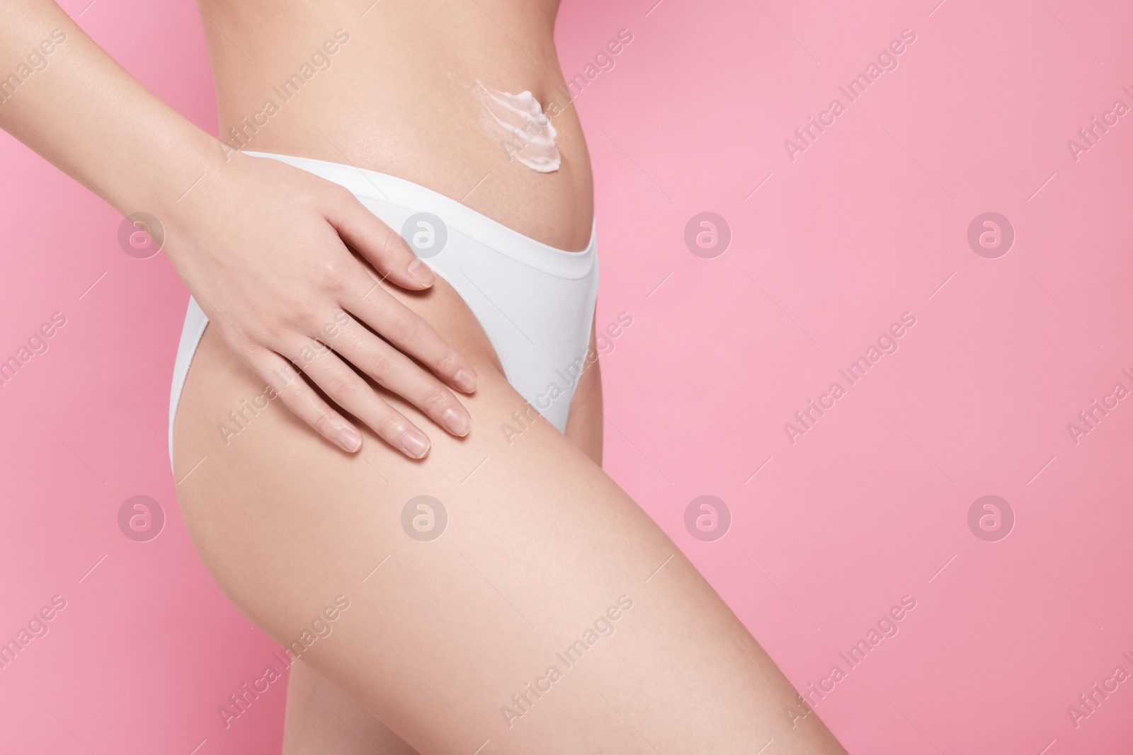 Photo of Woman with smear of body cream on belly against pink background, closeup. Space for text