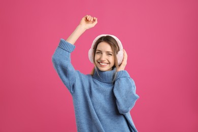 Photo of Happy woman wearing warm earmuffs on pink background