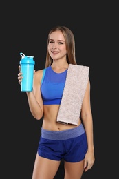 Photo of Portrait of woman with bottle of protein shake and towel on black background