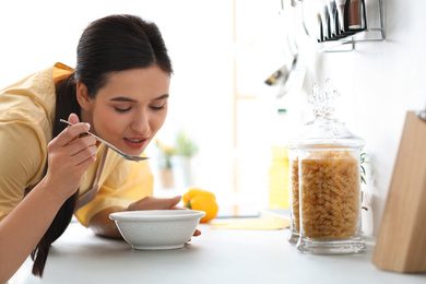 Young woman eating tasty soup at countertop in kitchen