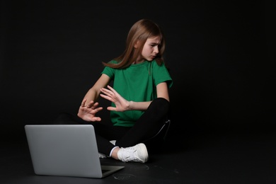 Photo of Scared teenage girl with laptop on black background. Danger of internet