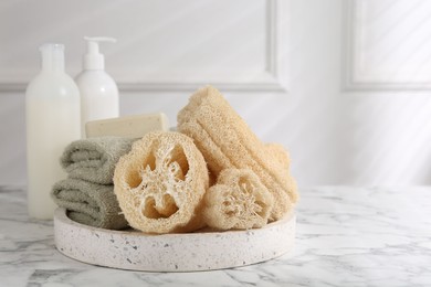 Photo of Loofah sponges, towels, soap and cosmetic products on white marble table, space for text