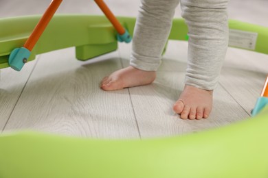Photo of Cute little boy making first steps with baby walker on wooden floor, closeup
