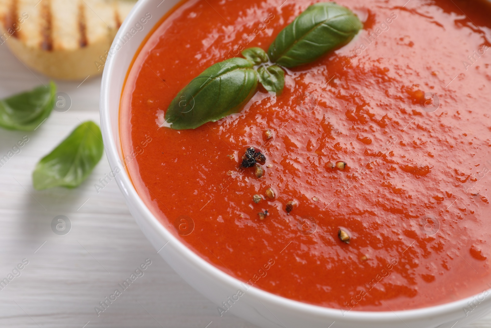 Photo of Delicious tomato cream soup in bowl on white wooden table, closeup