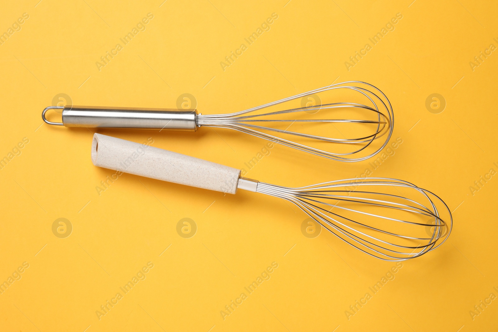 Photo of Two metal whisks on yellow background, top view
