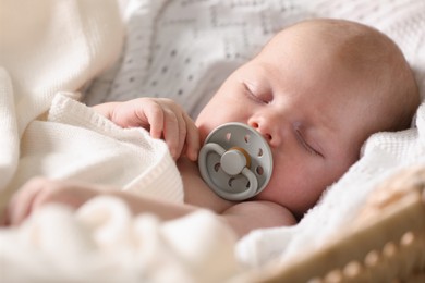 Cute newborn baby sleeping on white blanket in wicker crib, closeup