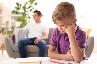 Upset child and blurred father on background. Family relationships