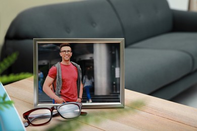 Photo of Framed photo of happy young man on wooden table in room. Space for text