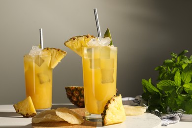 Photo of Tasty pineapple cocktails with ice cubes and delicious fruit on white table