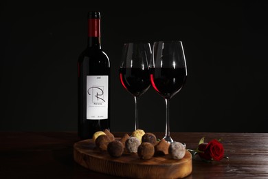 Photo of Red wine, chocolate truffles and rose flower on wooden table against dark background