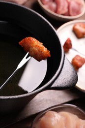Photo of Fondue pot and fork with fried meat piece on wooden table, closeup