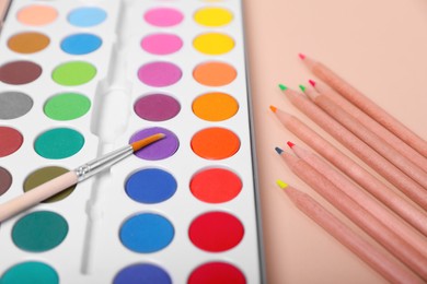 Photo of Watercolor palette with brush and colorful pencils on beige background, closeup