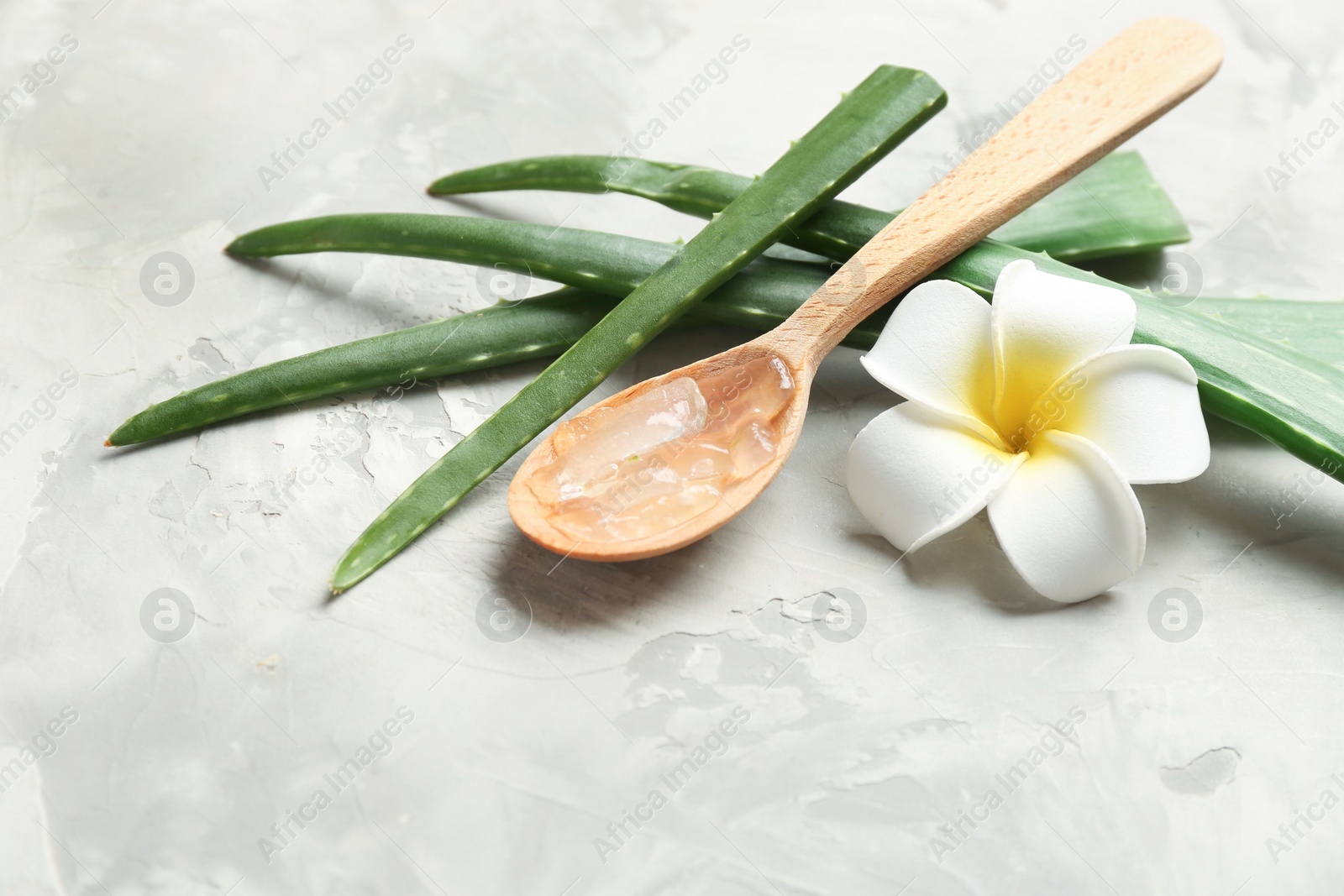 Photo of Slices of aloe vera, wooden spoon and flower on gray table