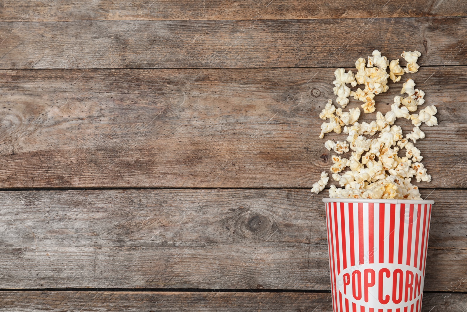 Photo of Overturned paper cup with tasty popcorn on wooden background, top view. Space for text