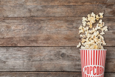 Overturned paper cup with tasty popcorn on wooden background, top view. Space for text