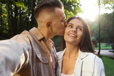 Photo of Affectionate young couple kissing and taking selfie in park