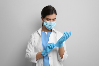 Photo of Doctor in protective mask putting on medical gloves against light grey background