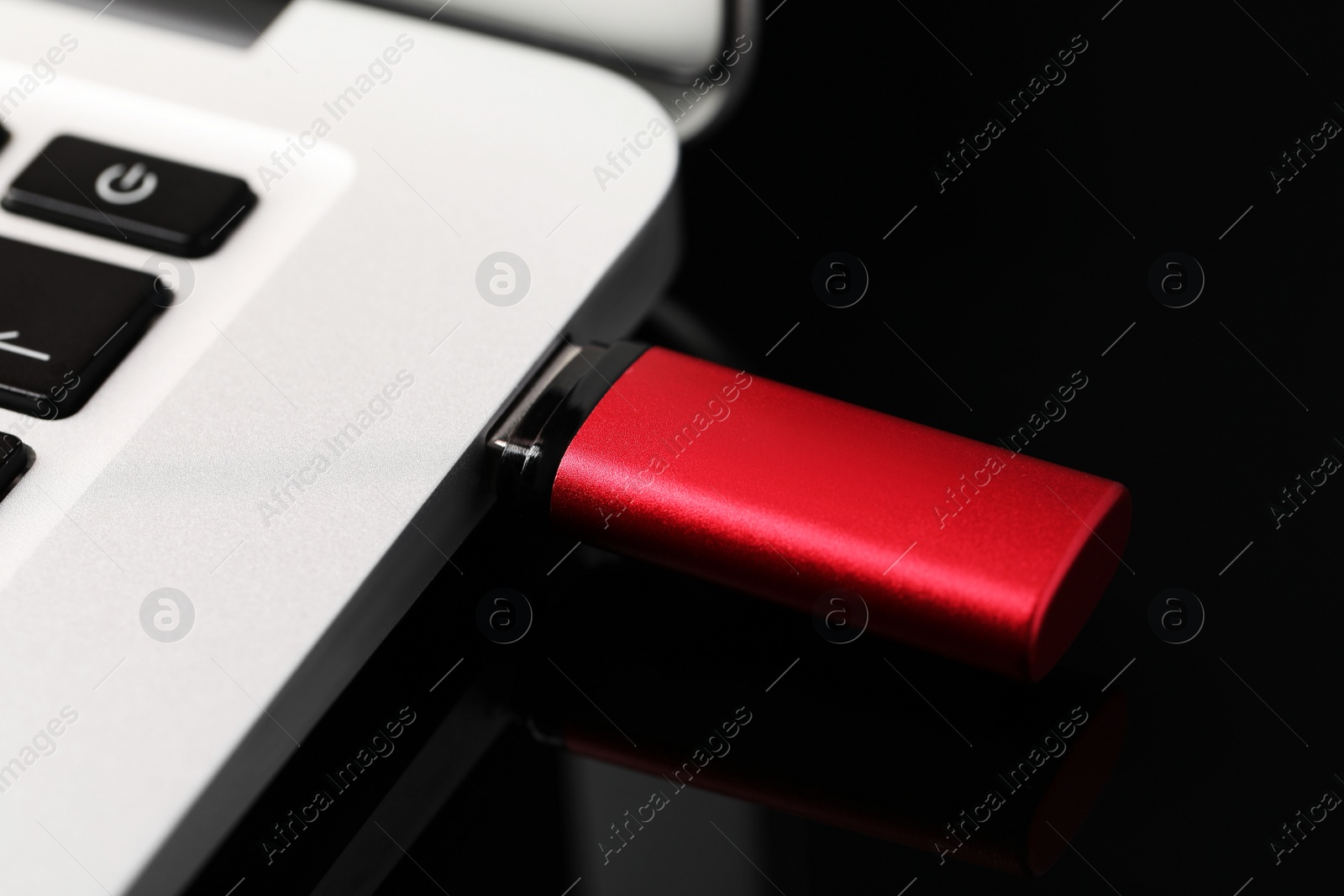 Photo of Modern usb flash drive attached into laptop on black table, closeup