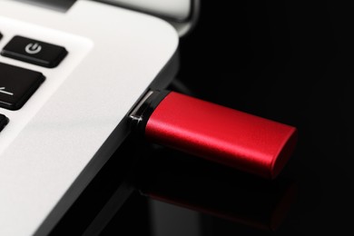 Photo of Modern usb flash drive attached into laptop on black table, closeup