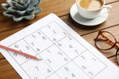 Photo of Sudoku, pencil, eyeglasses and cup of coffee on wooden table
