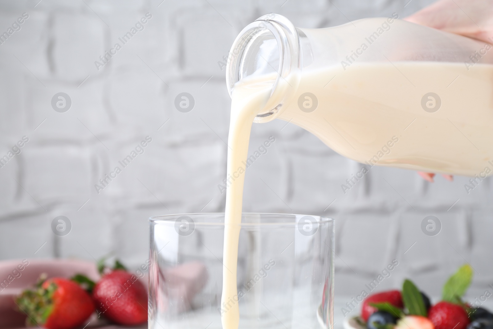 Photo of Woman pouring tasty yogurt into glass at table, closeup