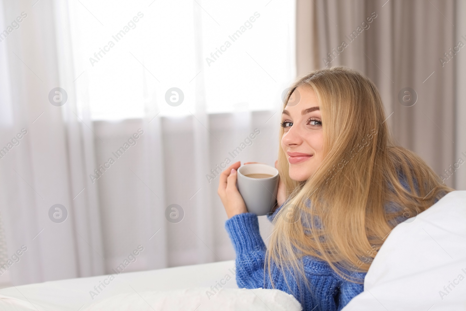 Photo of Beautiful young woman lying with cup in bed at home. Winter atmosphere