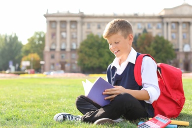 Schoolboy with stationery sitting on grass outdoors