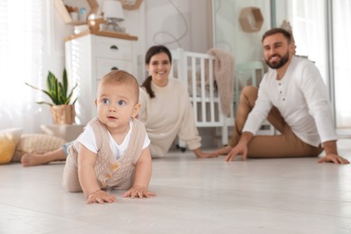 Happy parents watching their baby crawl on floor at home