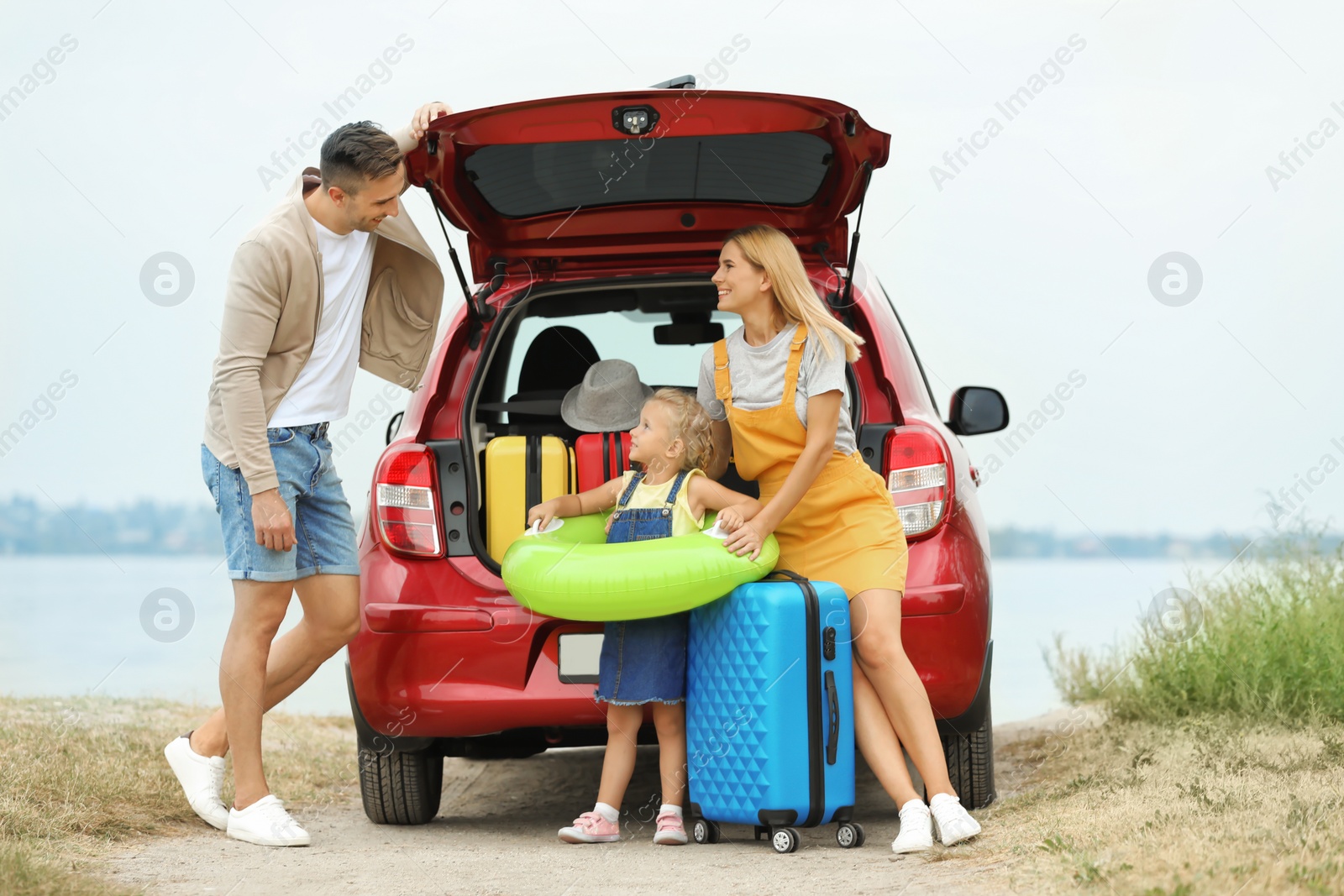 Photo of Happy family with suitcases and inflatable ring near car on riverside