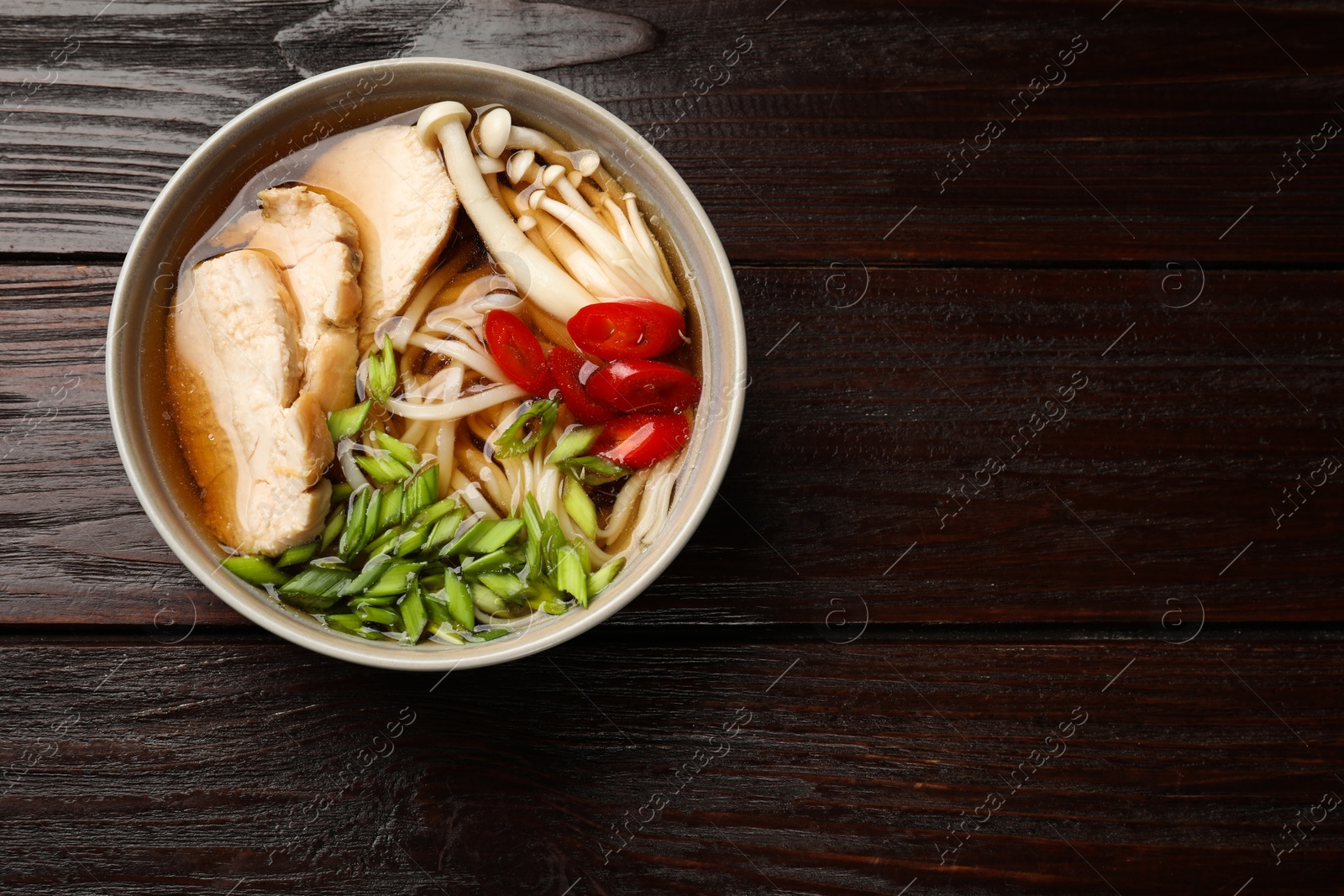 Photo of Delicious ramen with meat and mushrooms in bowl on wooden table, top view. Space for text