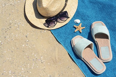 Stylish slippers, straw hat, sunglasses and blue towel on sand, space for text. Beach accessories